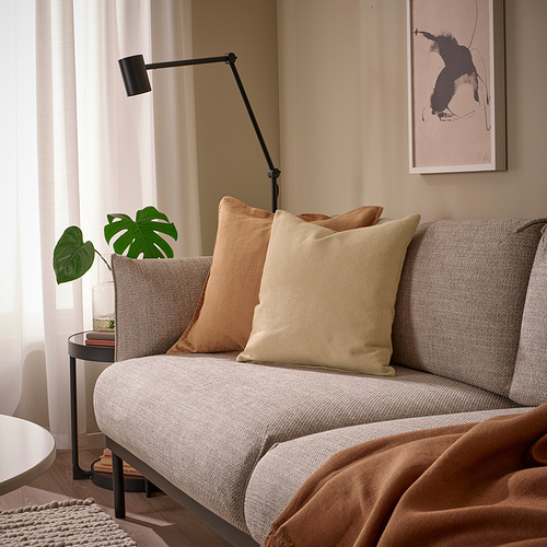 Cojín amarillo-beige sobre sofá gris, algodón reciclado y relleno de plumas, junto a la planta, decoración tranquila.