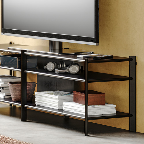 Moderno mueble de tv JÄTTESTA en color negro con estantes de bambú, con libros, auriculares y mandos a distancia.