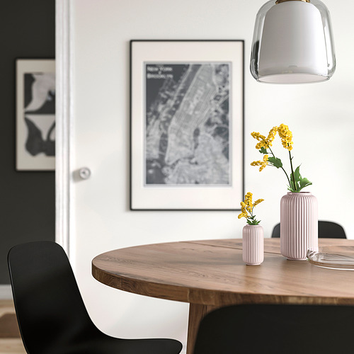 Mesa de comedor moderna con tapa de madera, sillas negras y lámpara colgante. Jarrones de gres a rayas rosas con flores amarillas. Cartel urbano de Nueva York detrás.