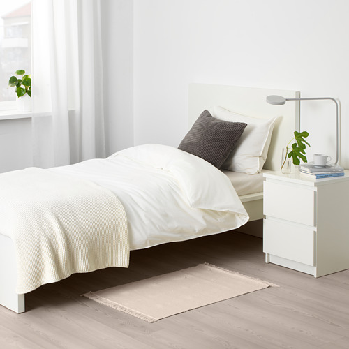 Dormitorio minimalista con alfombra beige, cama blanca y mesita de noche. Decoración neutra.