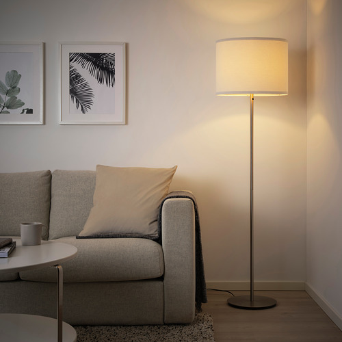 Acogedor salón comedor con lámpara de pie SKAFTET encendida junto a un sofá gris, destacando las luces de diseño moderno y tamaño.