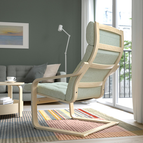 Sillón acolchado verde junto a ventana, con alfombra y mesa auxiliar.