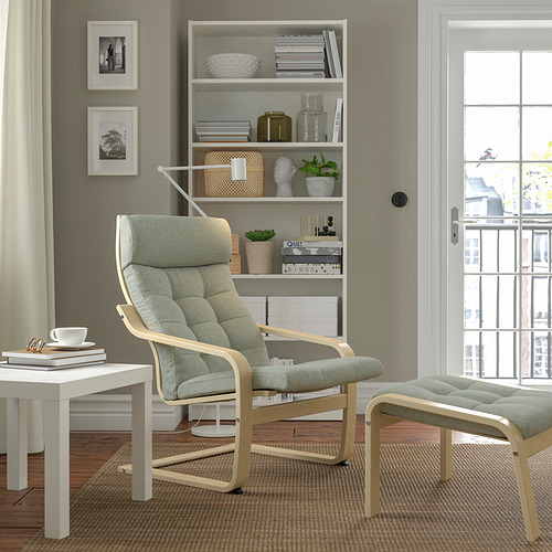 Acogedora sala de estar con sillón POÄNG, cojines, reposapiés, mesa auxiliar, estantería, plantas, vista a la ciudad.