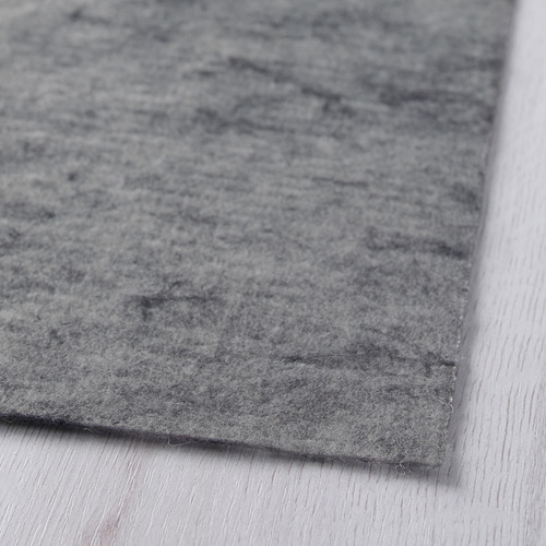 Primer plano de una alfombra gris suave y texturizada sobre una superficie de madera, mostrando su material afelpado de alta calidad.