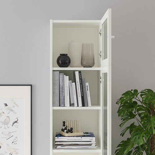 Una estantería blanca con puertas de vidrio, que muestra libros, jarrones y artículos decorativos. Dispone de estantes regulables y se ancla a la pared.