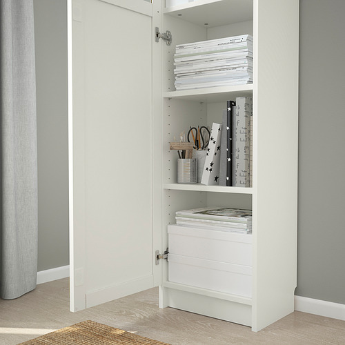 Estantería blanca BILLY con puertas de vidrio que exhibe libros cuidadosamente organizados, artículos decorativos y artículos de papelería en estantes.