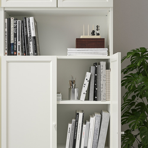 Estantería blanca con múltiples estantes que contienen libros y elementos decorativos como una planta, con estantes ajustables y puertas para el almacenamiento.