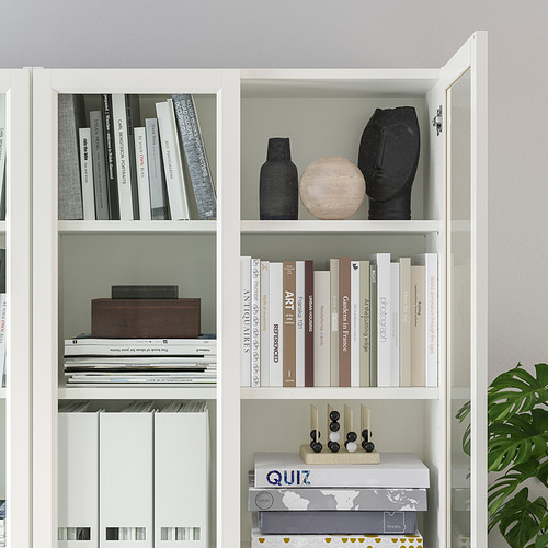 Librería blanca BILLY con estantes ajustables, que albergan libros y elementos decorativos como jarrones y una escultura de madera.