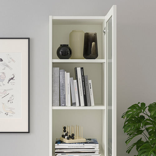 Estantería blanca BILLY con jarrones, libros y artículos decorativos en el estante inferior, un lado tiene puertas de vidrio.