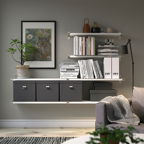 Sala de estar moderna con estante de pared que exhibe libros y decoración, que incluye arte de gatos, plantas y lámparas. Cajas de almacenamiento debajo y sofá con manta.
