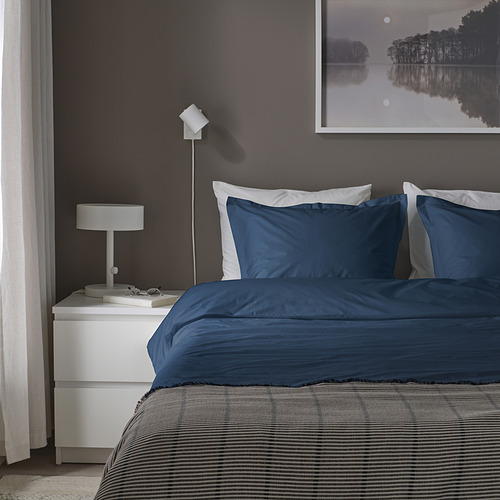 Juego de cama HAMPFLOCKEL azul oscuro de algodón, equipado con varias almohadas, colocado junto a una mesita de noche blanca con lámpara.