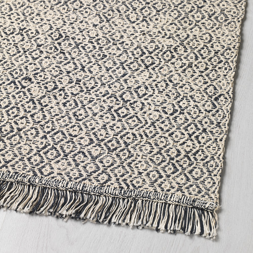 Alfombra tejida texturizada en blanco y negro con bordes de flecos, expuesta sobre una superficie plana.