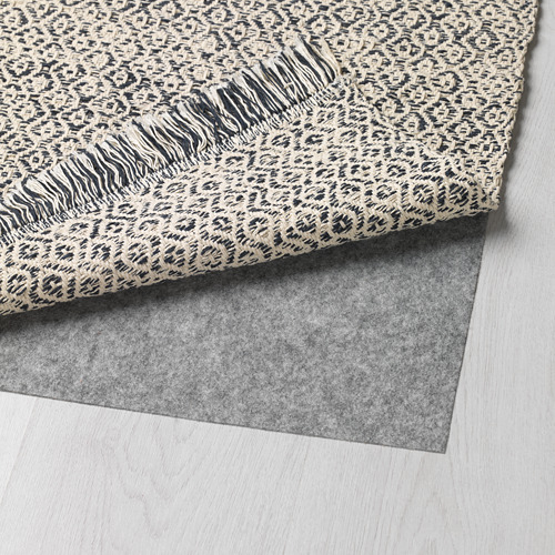 Una alfombra gris con estampado de leopardo se muestra enrollada sobre un suelo de madera clara, dejando al descubierto su parte trasera gris oscuro.