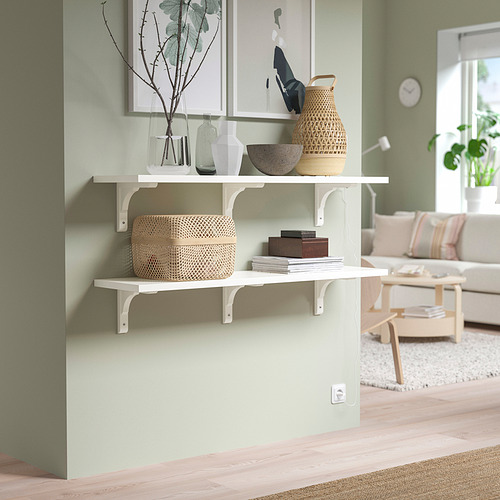 Estanterías de pared blancas BERGSHULT con cestas tejidas, jarrones y obras de arte enmarcadas. Salón luminoso y minimalista con suelo de madera clara.