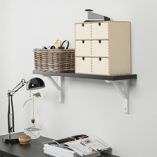 Estantería de pared con puertas de madera y una cesta con tijeras y gafas, junto a una lámpara de escritorio, un jarrón y revistas sobre un escritorio.
