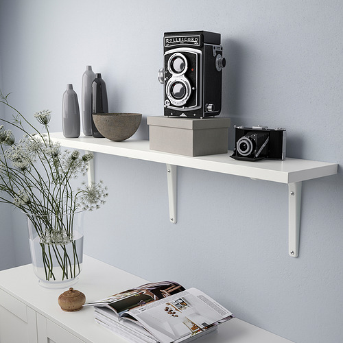 Estantería de pared blanca que exhibe cámaras y jarrones. Sujetado por soportes metálicos.