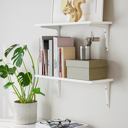 Estante blanco montado en la pared que contiene libros, una planta en maceta y una caja. Serie BURHULT, que ofrece un práctico almacenamiento y exposición.