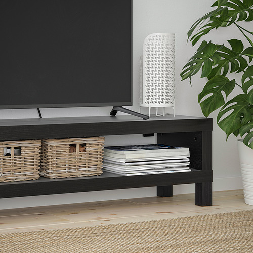 Mueble de tv NEGRO con cestas tejidas y libros apilados. Lámpara blanca y gran planta verde a su lado.