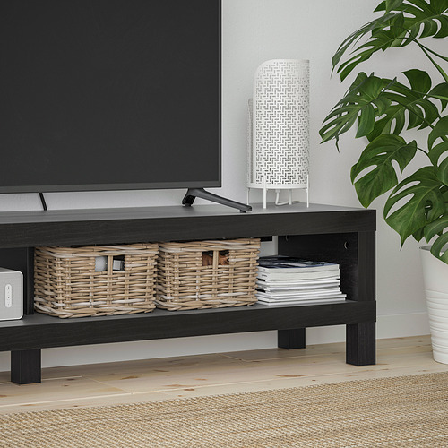 Banco de tv NEGRO con cestas tejidas y cds, junto a una gran planta frondosa.