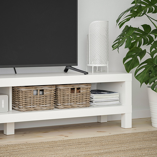 Mueble de TV blanco con almacenamiento de cesta, con un televisor de pantalla plana, libros y una lámpara decorativa.