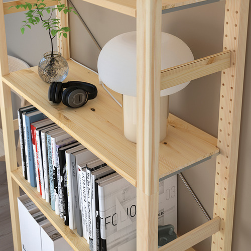 Estantería de madera clara con múltiples estantes que exhiben libros, auriculares, una pequeña maceta y una lámpara, que proporciona un almacenamiento y una organización versátiles.