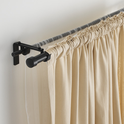 Barra de cortina ajustable negra con cortinas beige, asegurada por soportes de pared. Permite un fácil ajuste de la longitud, mejorando la decoración de la habitación.