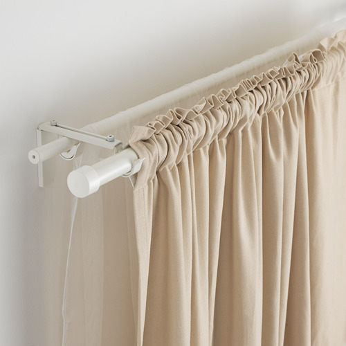 Barra de cortina de longitud ajustable, que sujeta cortinas de color beige. Varilla metálica flexible montada en la pared.