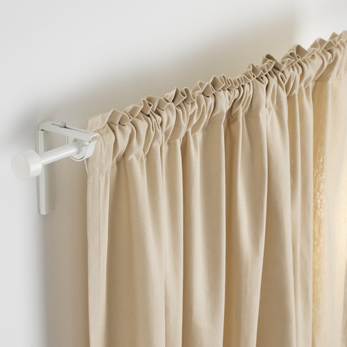Un primer plano de cortinas beige sobre una varilla metálica blanca ajustable, sostenida por soportes metálicos.