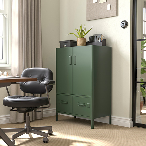 Armario de almacenamiento de metal verde IDÅSEN en la oficina junto a la silla y la ventana. Dos puertas, dos cajones, decorados con planta y suministros.
