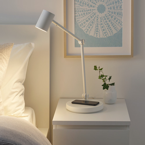 Lámpara NYMÅNE sobre mesa auxiliar, ajustable, cargador inalámbrico, diseño minimalista.