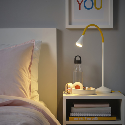 Dormitorio con cama, lámpara amarilla NÄVLINGE, botella de agua y libros.