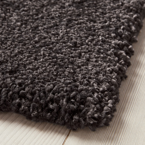 Alfombra peluda de color gris oscuro, pelo grueso y suave, sobre suelo de madera clara.