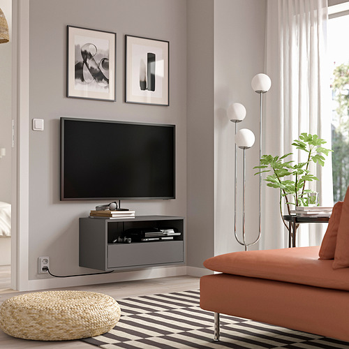 Sala de estar moderna con mueble de TV de pared EKET gris, pantalla plana y sofá naranja.