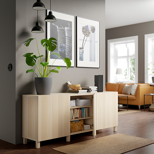 Salón moderno con aparador BESTÅ, planta, libros, decoración, fotos, sofá naranja.