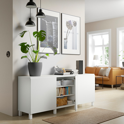 Sala de estar moderna con aparador BESTÅ, plantas, libros, decoración, lámparas colgantes negras y sofá naranja.