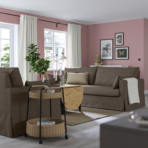Salón moderno con paredes rosas, sofás HYLTARP grises, mesa auxiliar de madera, cestas de mimbre y grandes ventanales con cortinas blancas.