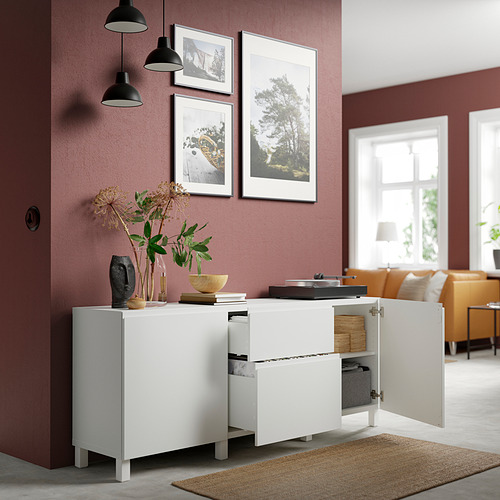 Mueble de almacenaje BESTÅ blanco con puertas abiertas, que revelan estantes y cajones ajustables. Colgando obras de arte y flores en la parte superior.