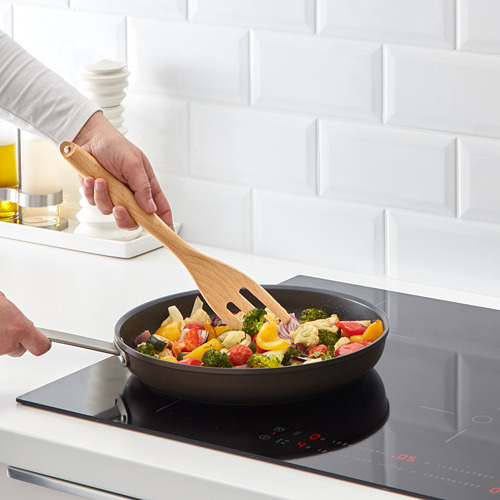 Persona revolviendo verduras de colores en una sartén antiadherente sobre una estufa de inducción.