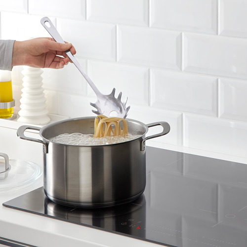 Persona cocinando pasta usando un servidor de espaguetis en una estufa.