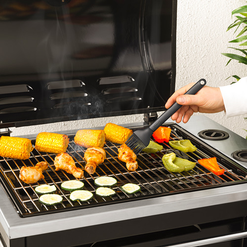 Persona asando alimentos con un cepillo, aplicando salsa. Maíz, pollo y verduras a la parrilla.