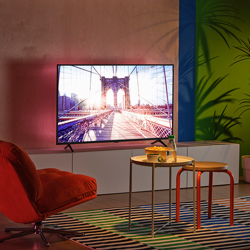 Sala de televisión moderna con decoración colorida, pantalla grande, silla naranja, paredes vibrantes, iluminación led, mesa pequeña con bocadillos.