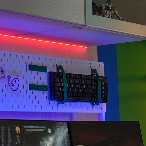 Tablero de clavijas montado en la pared con teclado, pegatinas y luces led de colores. Pequeña figura de acción en el estante.