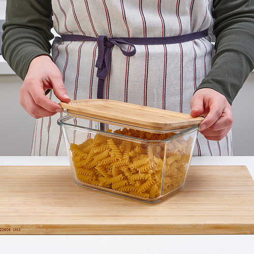 Una persona con delantal sostiene un recipiente de vidrio transparente lleno de pasta, mostrando su almacenamiento y visibilidad.