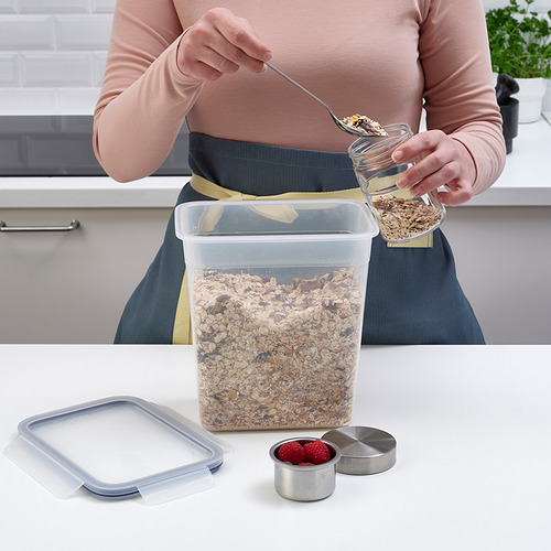 Una persona está sacando granola de un recipiente transparente de IKEA 365+ en la encimera de la cocina, que tiene una tapa con cierre a presión que garantiza la frescura y evita fugas.
