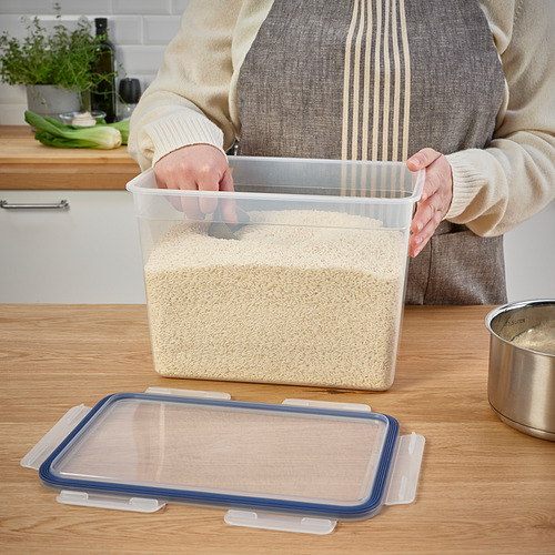 Persona que sostiene un gran recipiente transparente de alimentos lleno de granos, mostrando su tapa a prueba de fugas y su diseño apilable, ideal para el almacenamiento en la despensa.