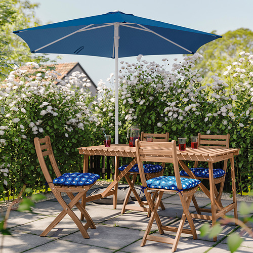 Patio al aire libre con cojines azules y sombrilla bajo árboles en flor.