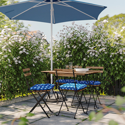 Configuración de patio con sillas acolchadas de lunares azules y blancos, mesa de madera y sombrilla azul marino bajo flores blancas en flor.