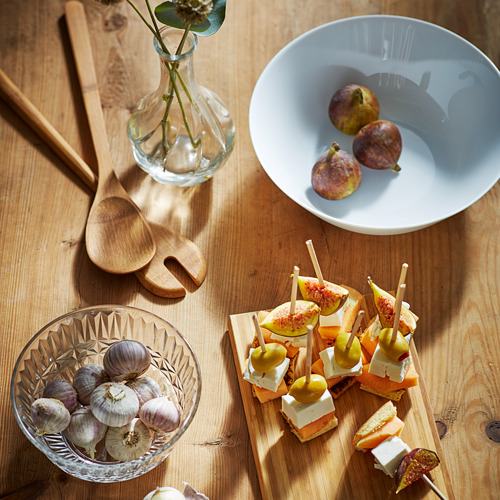 El juego de madera para servir incluye un tazón y una tabla de cortar con herramientas. Contiene fruta y aperitivos. Diseño simple y elegante.