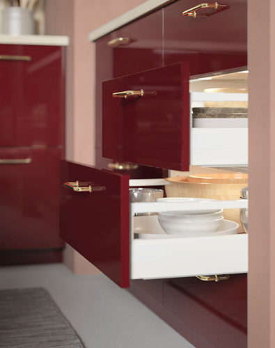 Cocina moderna con gabinetes rojos, manijas doradas y un cajón blanco abierto que revela tazones blancos. Se instalan pequeñas luces LED sobre el cajón.