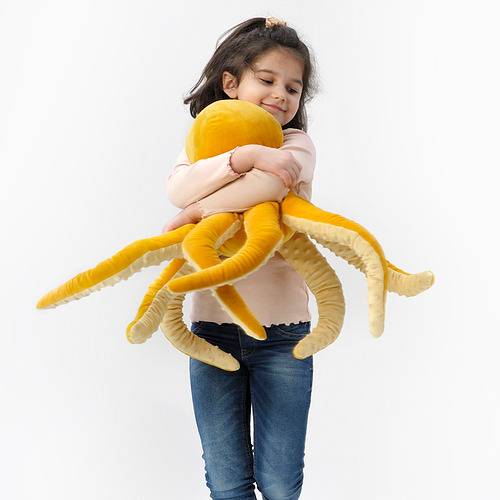 En un niño abraza un gran pulpo de peluche amarillo. El juguete tiene tentáculos suaves y largos y forma parte de la colección BLÅVINGAD.